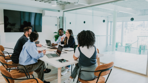 Group of people working in a bright sunny room with glass walls.