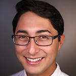 Gabe Abrams smiling brightly while wearing their black square glasses.