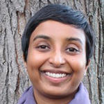 Sindhumathi Revuluri smiling in front of a tall tree trunk