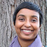 Sindhumathi Revuluri smiling in front of a tall tree trunk