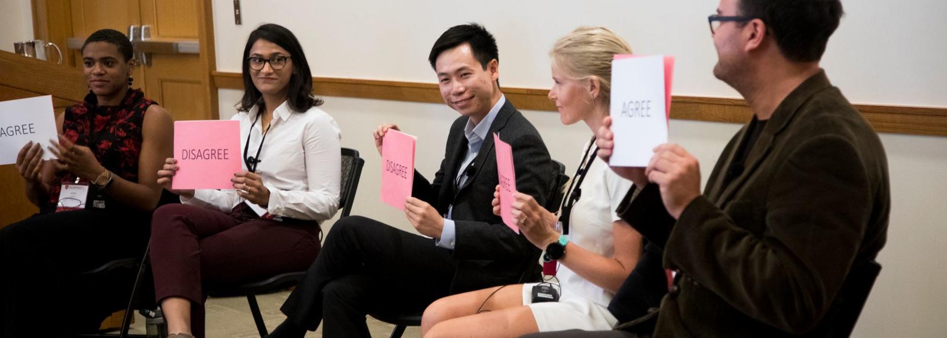 HILT 2018 conference panelist holding up pink and white signs.