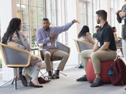 Colleagues talking in bright sunny room with grey and red chairs.