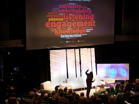 A person standing on stage pointing at a slide show