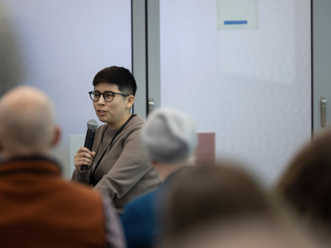 A person with short black hair speaking into a microphone 