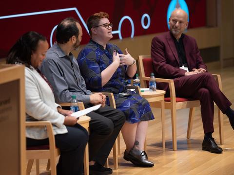A panel of educators on stage with red and tan chairs