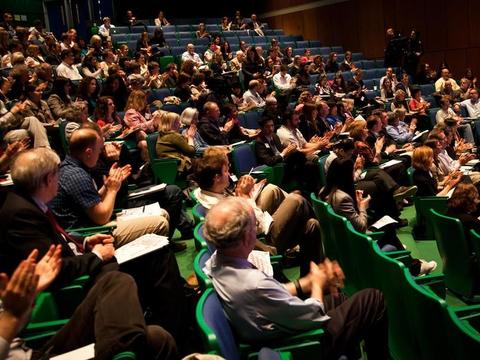 An audience sitting in green chairs