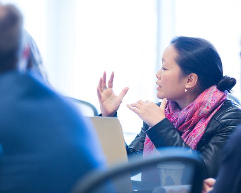 A woman wearing a beautiful pink scarf speaking with her hands during a HILT 2016 conference session.