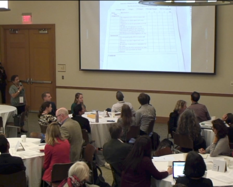 HILT Conference attendees in a room with a projector and white walls.