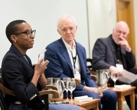 Three Harvard University educators sit on stage where a white backdrop hangs. 