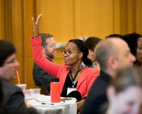 A woman wearing a bright red blazer as she raises her hand to answer a question.