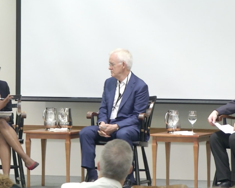 Three Harvard University educators sit on stage where a white backdrop hangs. 