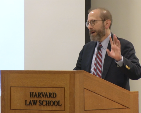 Allan Garber speaking into a microphone at a wooden Harvard podium.